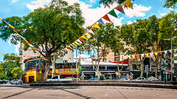 Praça em Palermo, com bandeirinhas coloridas instaladas e lojas ao fundo.