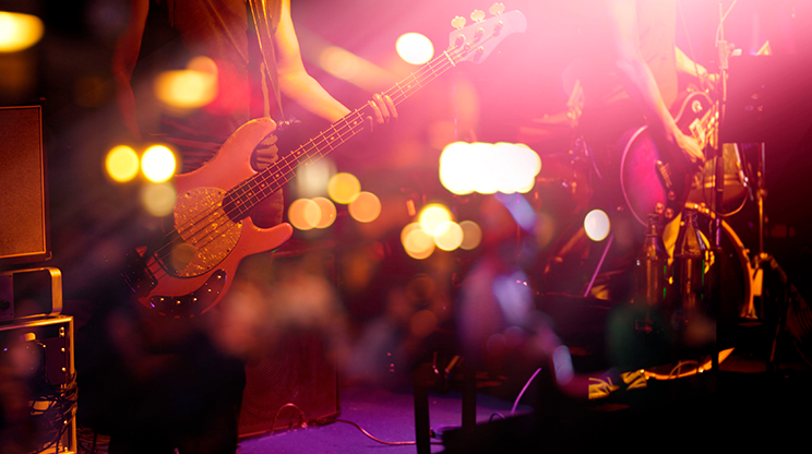 Palco de casa noturna na Barra Funda, com o baixista em primeiro plano, o guitarrista ao lado e parte da bateria. A imagem não mostra os rostos dos músicos. Atrás deles tem amplificadores e cabos pelo chão.