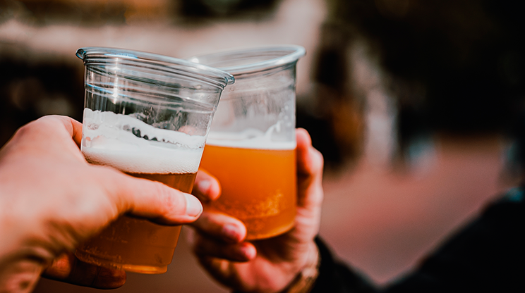 Dois copos de plástico cheios de cerveja se batem brindando em um bar de Cerqueira César.