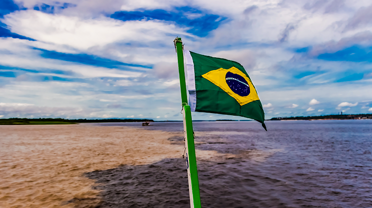 Encontro das águas do Rio Negro com Rio Solimões, em Manaus, com bandeira do Brasil em primeiro plano.