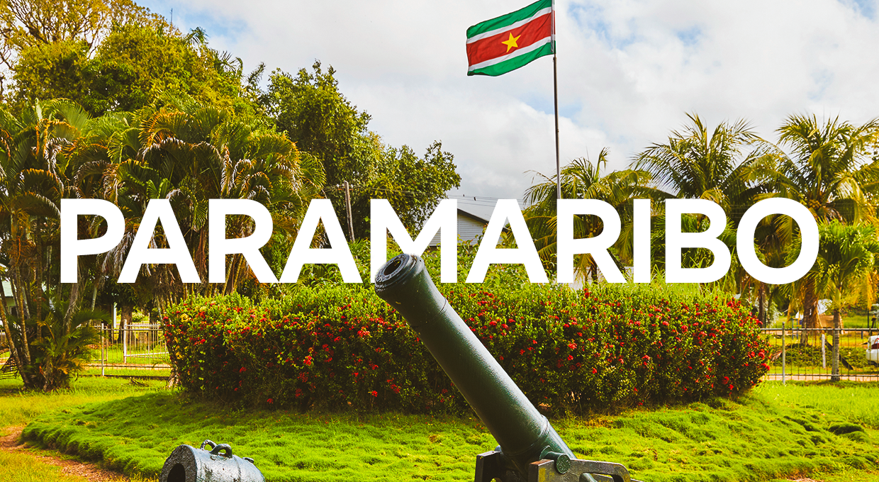 Distrito de Commewijne, com a bandeira da cidade e canhão antigo, e a palavra Paramaribo escrita em letras garrafais brancas.