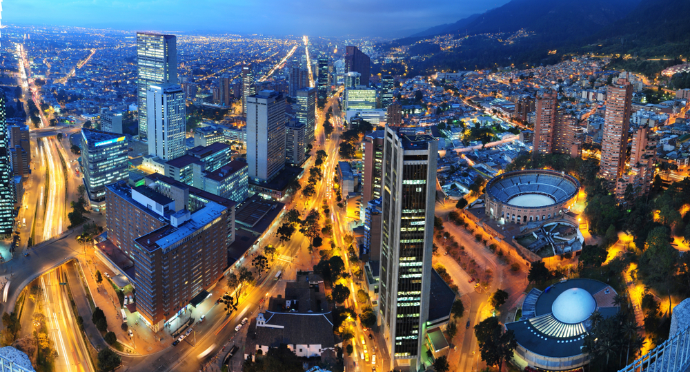 Imagem de Bogotá vista de cima à noite, com a iluminação de faróis dos carros, prédios e ruas.