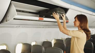 Image of a woman placing her luggage in the trunk above the seat.