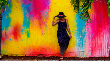 Mulher de chapéu cobrindo o rosto, encostada em um muro colorido do bairro cubano de Little Havana, em Miami.