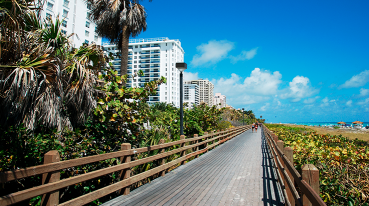 Calçadão de Miami Beach, rodeado de verde, edifícios de um lado e a praia de outro.
