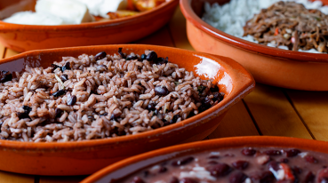 Travessas com comidas cubanas, sendo que em primeiro plano o prato leva arroz e feijão preto.