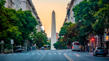 Imagem da Avenida Corrientes, com ônibus, carros e o Obelisco ao fundo.